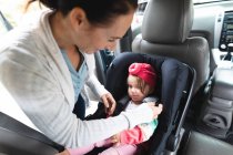Кавказька мати кладе своє дитя в безпечне дитяче крісло в машину. материнство, любов і догляд дітей — стокове фото