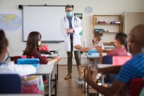 Caucasian male doctor showing how to use hand sanitizer to group of diverse students at school. health protection and safety at school during covid-19 pandemic concept — Stock Photo
