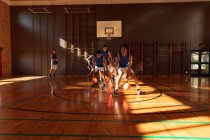 Разнообразная мужская баскетбольная команда в синей спортивной одежде и практикуется в дриблинге. баскетбол, спортивные тренировки на крытой площадке. — стоковое фото