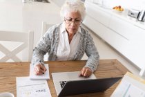 Змішана раса старша жінка сидить за столом, використовуючи ноутбук. перебування вдома в ізоляції під час карантину . — стокове фото
