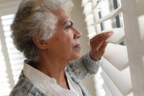 Mixed race senior woman looking through window. staying at home in isolation during quarantine lockdown. — Stock Photo