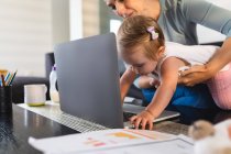 Caucasian mother holding her baby while she tries to touch the laptop at home. motherhood, love and baby care concept — Stock Photo