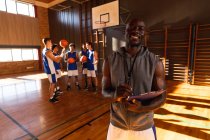 Portrait of african american male basketball coach with team in background. basketball, sports training at an indoor court during. — Stock Photo