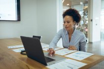 Gemischte Rasse Geschäftsfrau am Schreibtisch sitzend und mit Laptop. Arbeit in einem unabhängigen kreativen Unternehmen. — Stockfoto