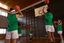 Equipe de basquete feminina diversa usando máscaras faciais e praticando tiro com bola. basquete, treinamento esportivo em um tribunal interno durante coronavírus covid 19 pandemia. — Fotografia de Stock