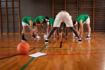 Diversos time de basquete feminino e treinador vestindo roupas esportivas e alongamento. basquete, treinamento esportivo em uma quadra interna. — Fotografia de Stock