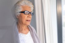 Femme âgée de race mixte regardant par la fenêtre. rester à la maison dans l'isolement pendant le confinement en quarantaine. — Photo de stock