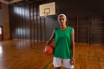 Portrait d'une joueuse de basket-ball mixte tenant le ballon. basket-ball, entraînement sportif sur un terrain intérieur. — Photo de stock