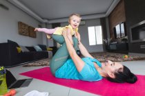Madre caucasica che tiene in braccio il suo bambino e fa yoga a casa. maternità, amore e concetto di cura del bambino — Foto stock