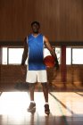 Retrato do jogador de basquetebol afro-americano que segura a bola. basquete, treinamento esportivo em uma quadra interna. — Fotografia de Stock
