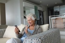 Mixed Race Seniorin sitzt auf dem Sofa und telefoniert per Smartphone. Isolationshaft während der Quarantäne. — Stockfoto