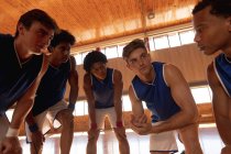 Разнообразная мужская баскетбольная команда и тренер по групповому обсуждению игровой тактики. баскетбол, спортивные тренировки на крытой площадке. — стоковое фото
