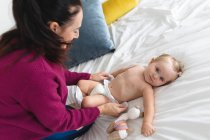 Madre caucásica cambiando pañales de su bebé en la cama en casa. maternidad, amor y cuidado del bebé - foto de stock