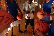Різноманітна чоловіча баскетбольна команда і тренер в хундлі обговорюють тактику гри. баскетбол, спортивне тренування в критому дворі . — стокове фото