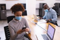 Дві різні чоловічі та жіночі бізнес-колеги носять маски для обличчя, використовуючи ноутбук та смартфон. робота в сучасному офісі під час пандемії коронавірусу 19 . — стокове фото