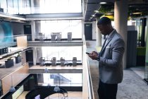 Uomo d'affari afroamericano che utilizza lo smartphone mentre si trova nel corridoio in un ufficio moderno. concetto di business e ufficio — Foto stock