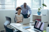 Zwei unterschiedliche männliche und weibliche Kollegen sitzen am Schreibtisch, lächeln und benutzen Laptop. Arbeit in einem unabhängigen kreativen Unternehmen. — Stockfoto