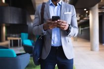 Средняя часть африканского американского бизнесмена использует смартфон, стоя в современном офисе. бизнес и офисная концепция — стоковое фото