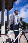 Pensativo empresário afro-americano com bicicleta em pé em um parque corporativo. conceito de negócio e escritório — Fotografia de Stock