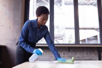 Африканська американка чистить стіл дезінфікуючим розпилювачем і тканиною в кафе. очищення та дезінфекція для профілактики та контролю епідемії ковини-19 — стокове фото