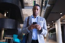 Homme d'affaires afro-américain utilisant un smartphone tout en étant debout au bureau moderne. concept d'entreprise et de bureau — Photo de stock