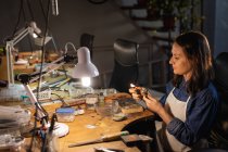 Mulher branca joalheiro sentado na mesa, segurando ferramentas de jóias, fazendo jóias na oficina. negócios artesanais independentes. — Fotografia de Stock