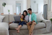 Sorrindo mãe hispânica, pai e filha sentados no sofá usando laptop juntos. família passar tempo juntos em casa. — Fotografia de Stock