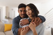 Porträt eines glücklichen hispanischen Paares, das sich im Wohnzimmer umarmt und in die Kamera blickt. Zuhause in Isolation während der Quarantäne. — Stockfoto