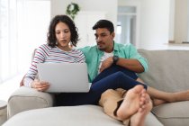 Pareja hispana relajándose en el sofá usando un ordenador portátil juntos. familia pasar tiempo juntos en casa. - foto de stock