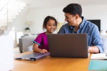 Посміхаючись, його батько і дочка сидять у вітальні, використовуючи ноутбук разом. сім'я проводить час разом вдома . — стокове фото
