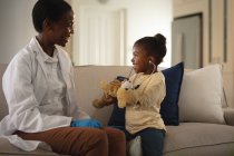 Médecine afro-américaine souriante visitant une patiente à la maison, jouant avec un stéthoscope. services médicaux et de santé, visite à domicile chez le médecin. — Photo de stock