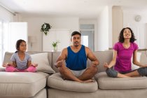 Glückliche hispanische Tochter und Eltern, die Yoga praktizieren, sitzen auf der Couch im Wohnzimmer. Zuhause in Isolation während der Quarantäne. — Stockfoto