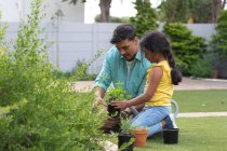 Sonriente padre hispano e hija jardinería, arrodillándose y plantando en macizo de flores. familia pasar tiempo juntos en casa. - foto de stock