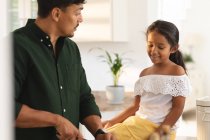 Happy hispanic daughter and father preparing food in kitchen, daughter sitting on counter. at home in isolation during quarantine lockdown. — Stock Photo