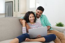 Smiling hispanic couple sitting on couch using laptop together. family spending time together at home. — Stock Photo