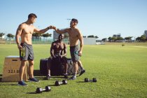 Diverso gruppo di uomini felici senza maglietta che si esercitano all'aperto, facendo una pausa a parlare e battendo pugni. sano stile di vita attivo, cross training per il fitness. — Foto stock