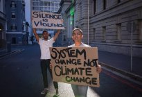 Two mixed race male friends carrying hand painted protest signs with slogans walking in city street. equal rights and justice protestors demonstrating in city. — Stock Photo