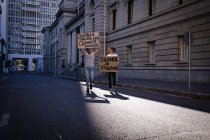 Zwei männliche Freunde gemischter Rassen mit handgemalten Protestschildern laufen durch die Straßen der Stadt. Demonstranten für gleiche Rechte und Gerechtigkeit demonstrieren in der Stadt. — Stockfoto