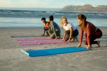 Група різноманітних друзів-жінок, які практикують йогу, розкладають килимки на пляжі. здоровий активний спосіб життя, фітнес на відкритому повітрі та благополуччя . — стокове фото