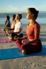 Groupe d'amies diverses pratiquant le yoga, méditant à la plage. mode de vie sain et actif, forme physique extérieure et bien-être. — Photo de stock