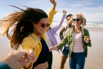 Happy group of diverse female friends having fun, walking along beach holding hands and laughing. holiday, freedom and leisure time outdoors. — Stock Photo
