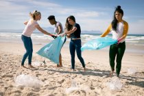 Diverse Frauen laufen am Strand entlang und sammeln Plastikmüll auf. Freiwillige Umweltschützer, Säuberung des Strandes. — Stockfoto