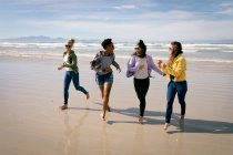Щаслива група різноманітних друзів розважається, гуляє вздовж пляжу та сміється. свято, свобода і дозвілля на відкритому повітрі . — стокове фото