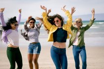 Grupo feliz de amigas divertidas se divertindo, andando ao longo da praia de mãos dadas e rindo. férias, liberdade e lazer ao ar livre. — Fotografia de Stock
