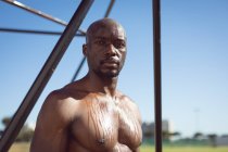 Portrait of fit shirtless african american man exercising outdoors, taking a break by exercise frame. healthy active lifestyle, cross training for fitness. — Stock Photo