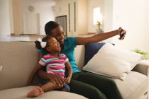 Bonne mère afro-américaine et sa fille se détendre sur le canapé et prendre selfie. passer du temps ensemble à la maison. — Photo de stock