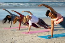 Група різноманітних друзів-жінок, які практикують йогу, спираючись на одну руку, що тягнеться на пляжі. здоровий активний спосіб життя, фітнес на відкритому повітрі та благополуччя . — стокове фото