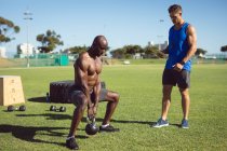 Afrikanisch-amerikanischer muskulöser Mann, der im Freien mit Wasserkocher-Glocken und Fitnesstrainer trainiert. gesunder aktiver Lebensstil, Crosstraining für Fitness. — Stockfoto