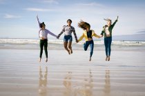 Fröhliche Gruppe unterschiedlicher Freundinnen, die Spaß haben, Händchen haltend am Strand spazieren gehen und springen. Urlaub, Freiheit und Freizeit im Freien. — Stockfoto