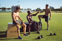 Grupo diverso de homens felizes sem camisa se exercitando ao ar livre, fazendo uma pausa falando e batendo punhos. estilo de vida ativo saudável, treinamento cruzado para fitness. — Fotografia de Stock